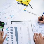 Colleagues collaborating on financial charts and graphs using mobile and paper documents in the office. — Cool Large Spaces E
