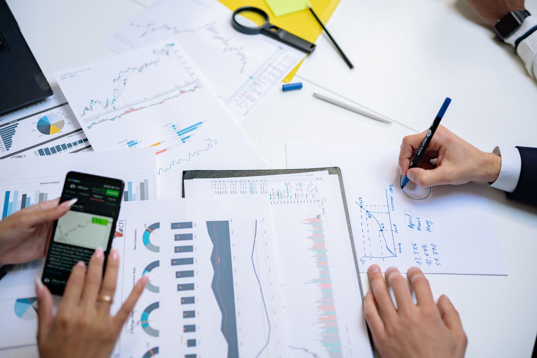 Colleagues collaborating on financial charts and graphs using mobile and paper documents in the office. — Cool Large Spaces E