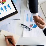 Business professionals handshake over graphs and charts in a corporate setting, symbolizing successful negotiation and agreem