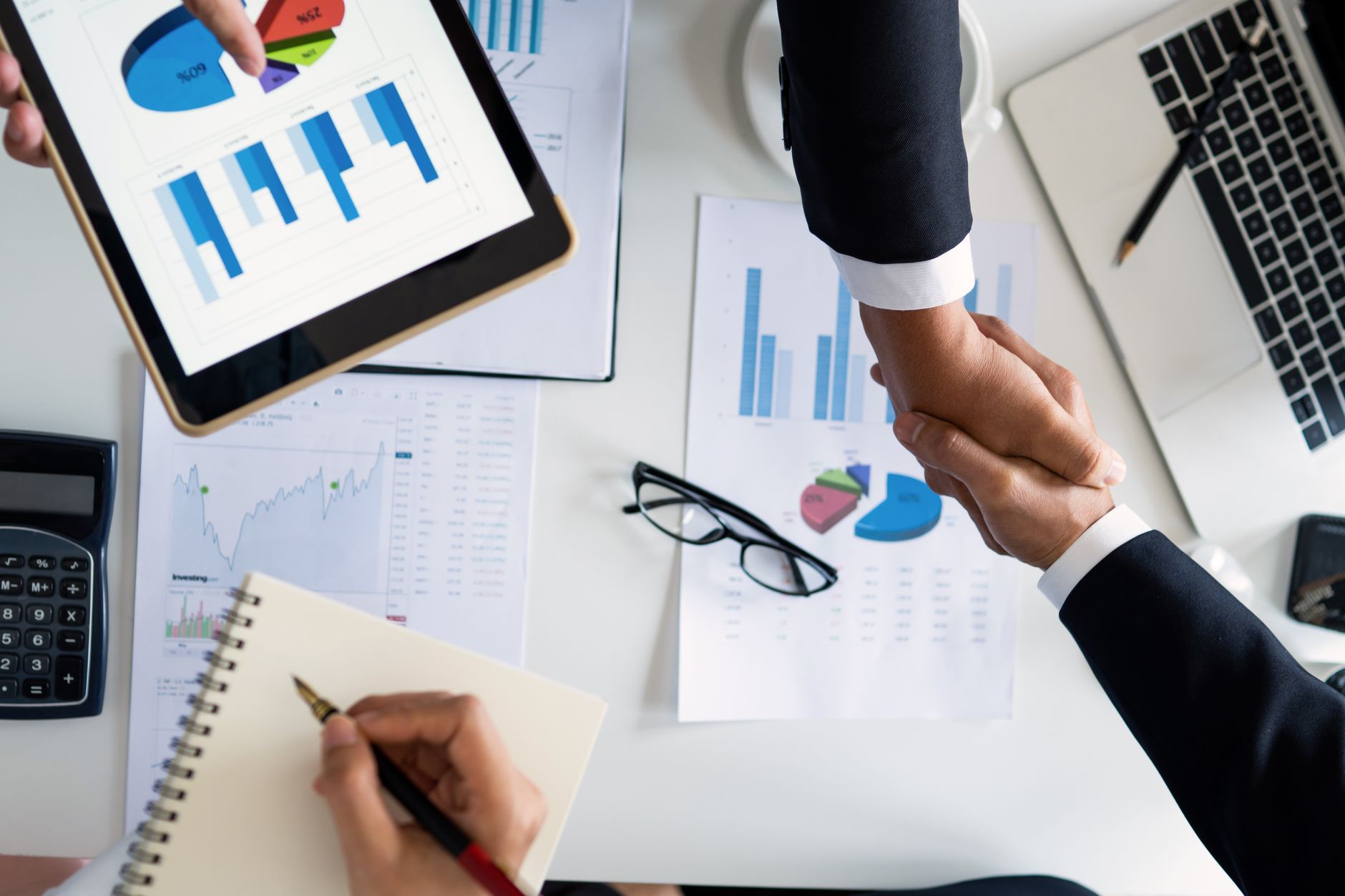 Business professionals handshake over graphs and charts in a corporate setting, symbolizing successful negotiation and agreem