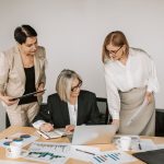 Three businesswomen discussing documents during a meeting in a modern office setting. — Navigating Testosterone Pricing: Fact