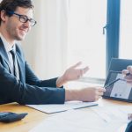 Two businessmen in formal attire discussing a business report in an office setting with a tablet. — Total casino login