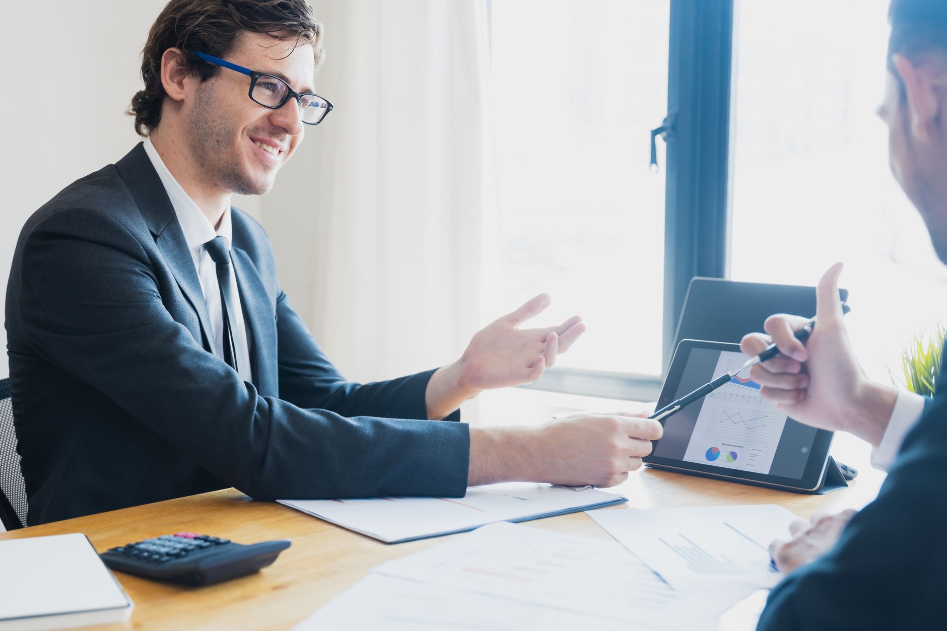 Two businessmen in formal attire discussing a business report in an office setting with a tablet. — Total casino login